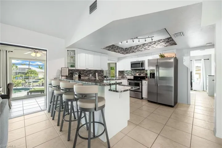 Kitchen featuring appliances with stainless steel finishes, backsplash, track lighting, kitchen peninsula, and light tile patterned flooring