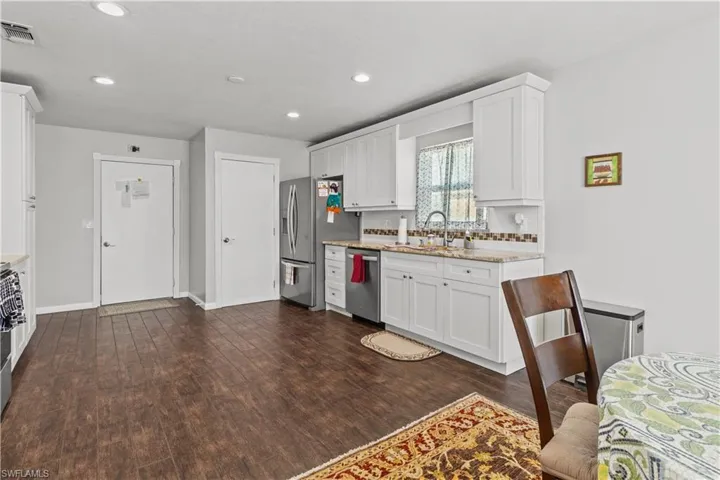 Kitchen with appliances with stainless steel finishes, white cabinetry, sink, light stone counters, and dark hardwood / wood-style flooring