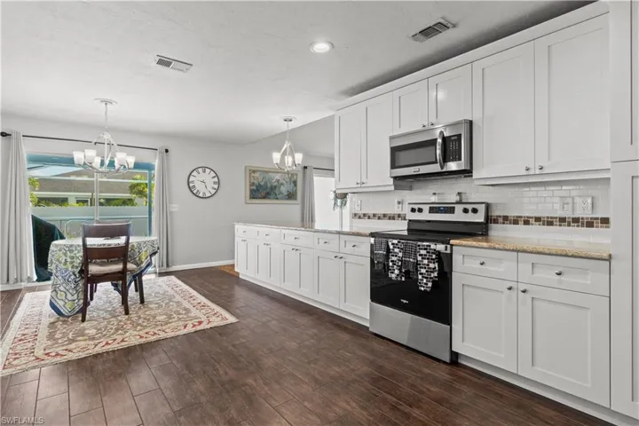 Kitchen with backsplash, an inviting chandelier, appliances with stainless steel finishes, dark wood-type flooring, and white cabinets