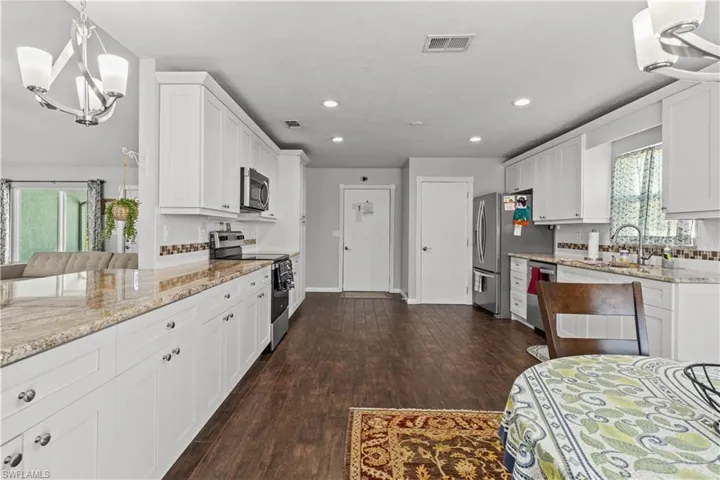 Kitchen featuring backsplash, stainless steel appliances, white cabinetry, light stone countertops, and dark wood-type flooring