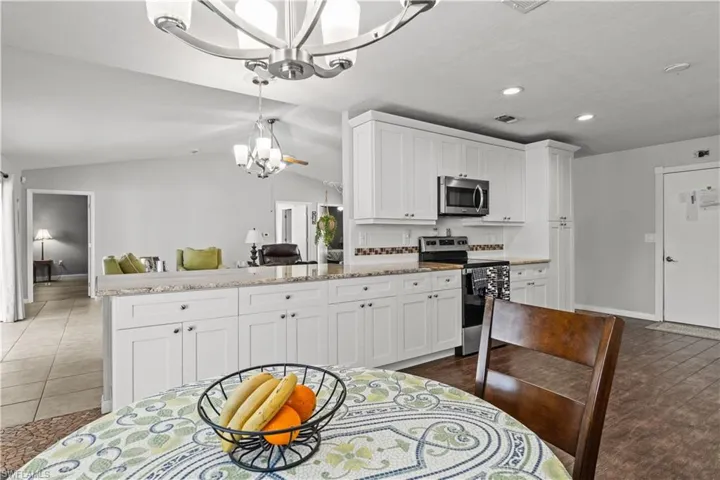 Kitchen with appliances with stainless steel finishes, lofted ceiling, white cabinetry, and an inviting chandelier