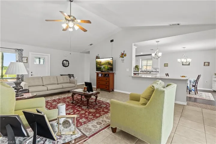 Tiled living room featuring plenty of natural light, lofted ceiling, and ceiling fan with notable chandelier