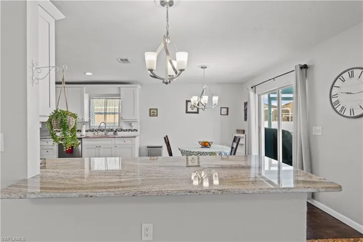 Kitchen with white cabinets, dark wood-type flooring, light stone counters, and a healthy amount of sunlight