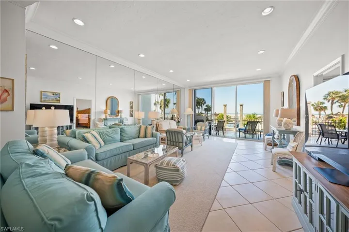 Tiled living room featuring crown molding, volume ceilings, expansive mirrored wall, view of the porch/lanai, pool and the Gulf of Mexico beyond...
