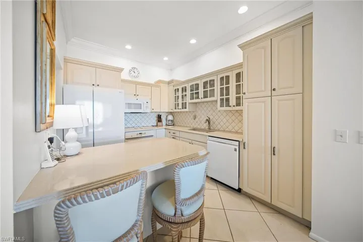 Equipped Kitchen featuring white appliances, a breakfast bar area, light tile patterned floors, and pillow tile  backsplash
