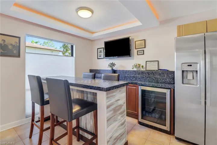 Bar with a raised ceiling, stainless steel fridge with ice dispenser, light tile patterned floors, and beverage cooler