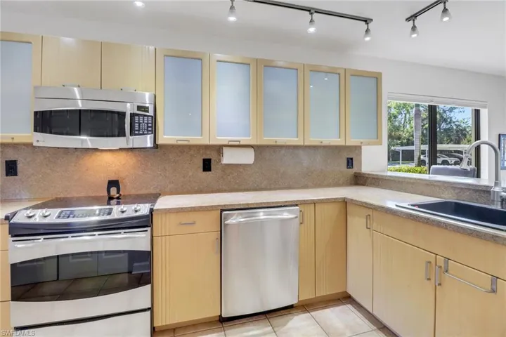 Kitchen featuring light tile patterned floors, light brown cabinetry, sink, and appliances with stainless steel finishes