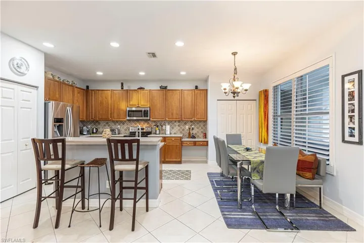 Kitchen with light tile patterned floors, appliances with stainless steel finishes, an island with sink, hanging light fixtures, and a chandelier