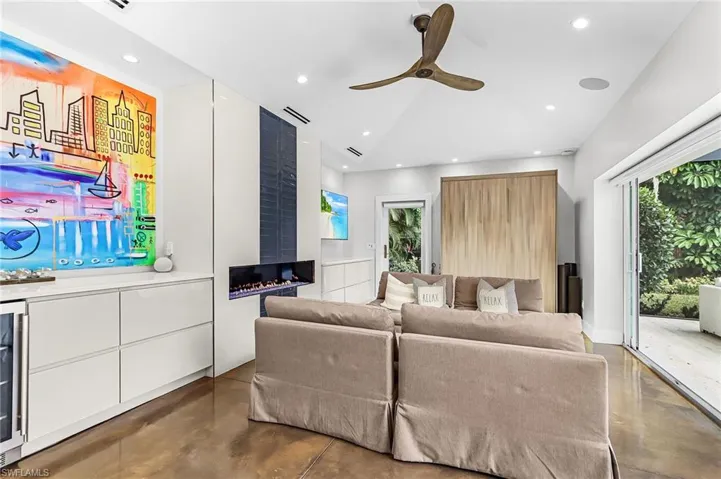 Living room with concrete floors, a ceiling fan, a fireplace, wine cooler, and recessed lighting