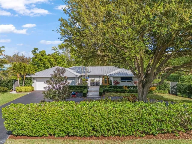 Single story home with a garage, asphalt driveway, a standing seam roof, and a porch