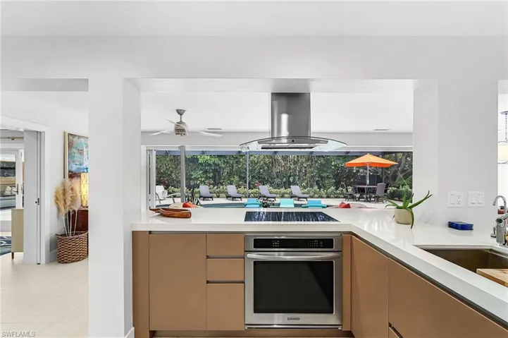 Kitchen with stainless steel oven, island exhaust hood, light stone countertops, a ceiling fan, and black electric stovetop