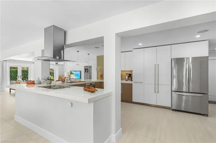 Kitchen with freestanding refrigerator, island exhaust hood, white cabinetry, modern cabinets, and light tile patterned floors