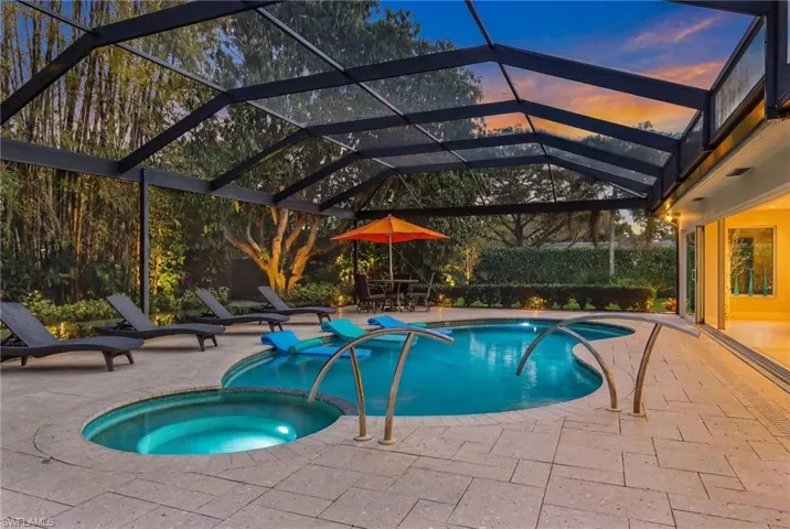 Pool at dusk featuring a sunroom, glass enclosure, a pool with connected hot tub, and a patio area