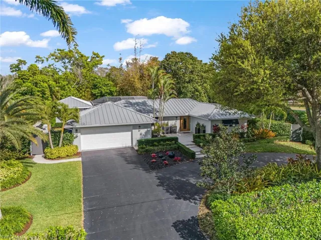 Ranch-style house with an attached garage, asphalt driveway, a front yard, and view of scattered trees