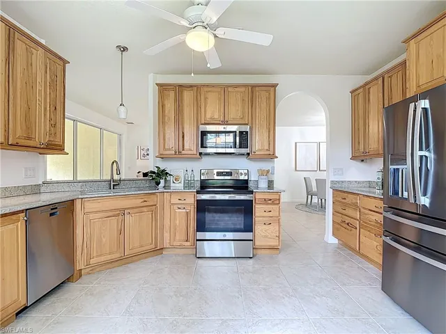 Kitchen with arched walkways, stainless steel appliances, ceiling fan, pendant lighting, and light stone counters