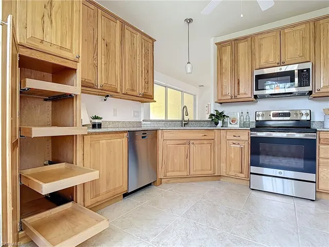 Kitchen featuring open shelves, appliances with stainless steel finishes, light stone countertops, and pendant lighting