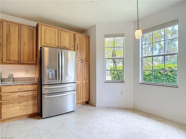 Kitchen featuring stainless steel fridge with ice dispenser, light stone countertops, hanging light fixtures, and brown cabinetry