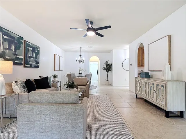 Living area with arched walkways, light tile patterned floors, a chandelier, and a ceiling fan