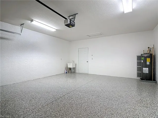 Garage featuring water heater, a garage door opener, and a textured wall