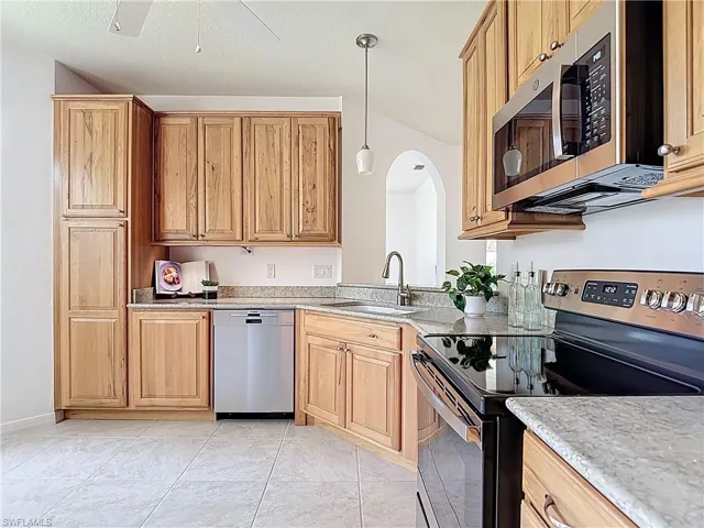Kitchen with appliances with stainless steel finishes, arched walkways, hanging light fixtures, a ceiling fan, and light stone counters