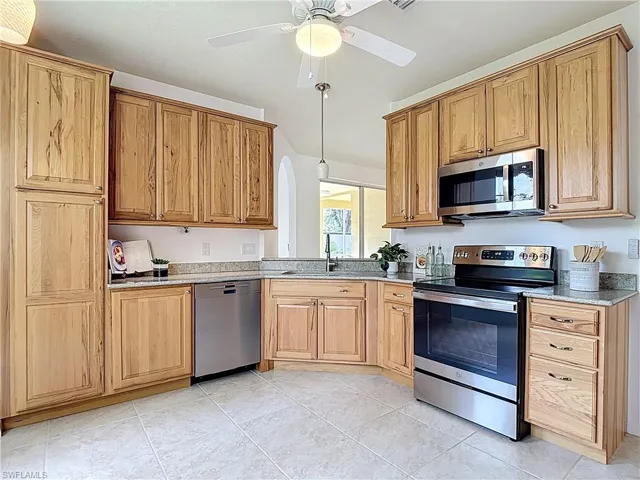 Kitchen with stainless steel appliances, light stone countertops, ceiling fan, arched walkways, and light tile patterned floors