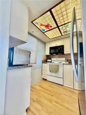 Kitchen with white range with electric cooktop, freestanding refrigerator, white cabinetry, and black microwave