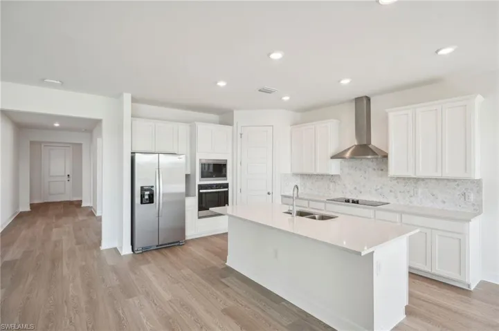 Kitchen with light hardwood / wood-style floors, sink, white cabinetry, wall chimney range hood, and appliances with stainless steel finishes