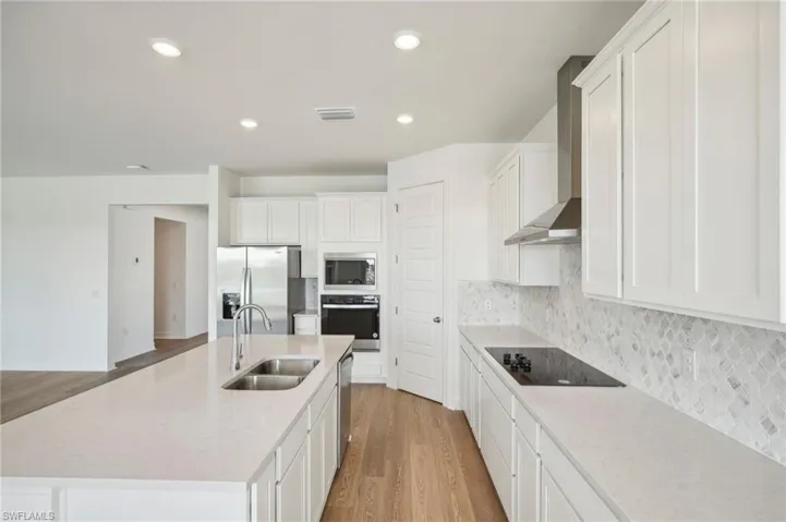 Kitchen featuring stainless steel appliances, light hardwood / wood-style flooring, a kitchen island with sink, sink, and wall chimney range hood