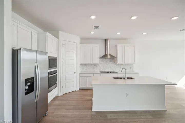 Kitchen with sink, white cabinets, wall chimney range hood, a center island with sink, and appliances with stainless steel finishes