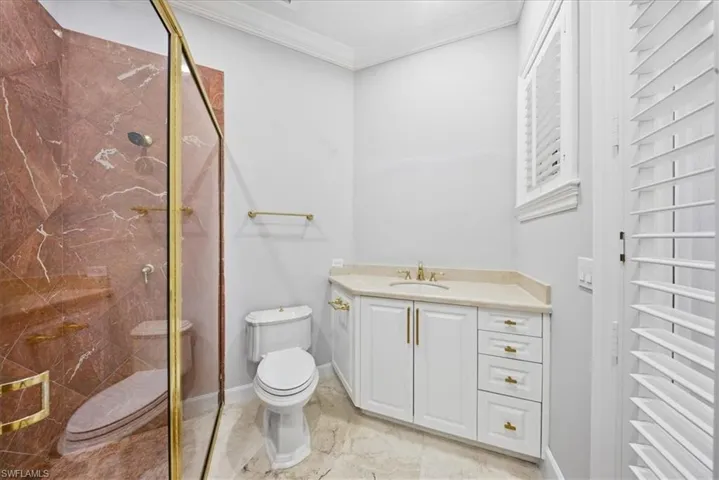 Full bath featuring crown molding, vanity, a marble finish shower, and light marble finish floors