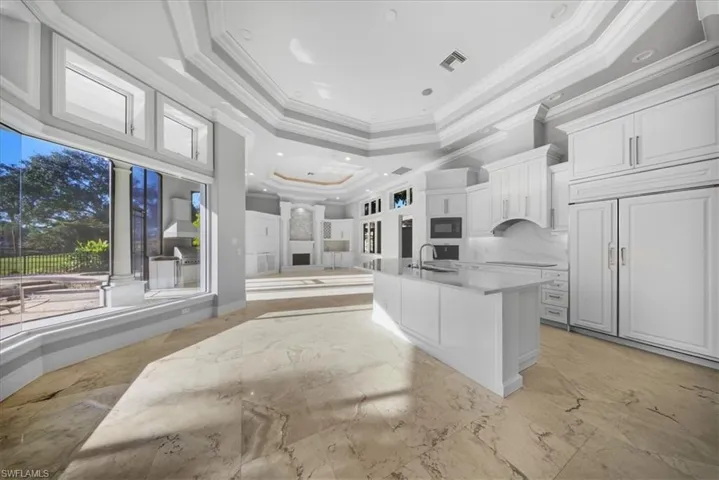 Kitchen featuring open floor plan, light marble finish floors, a kitchen island with sink, ornamental molding, and white cabinetry