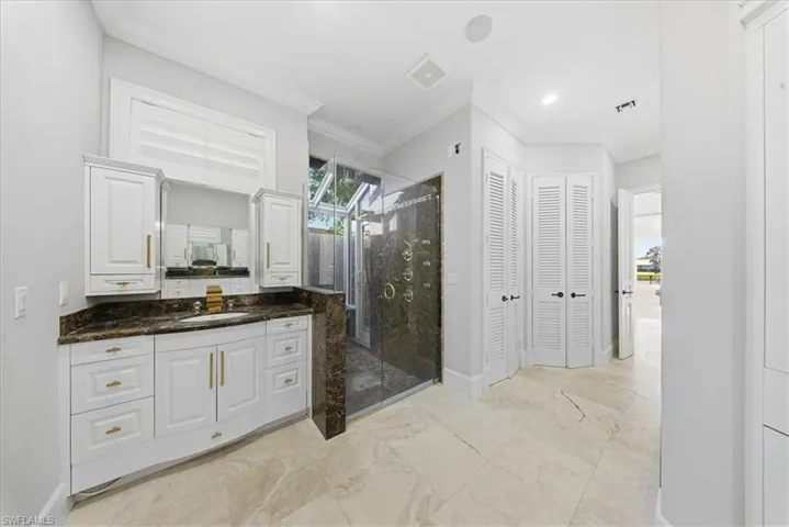 Bathroom with a closet, vanity, a shower stall, and ornamental molding