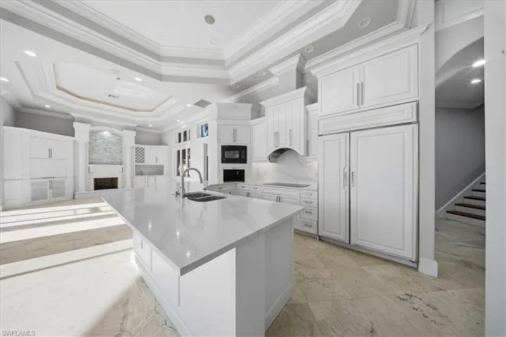 Kitchen featuring a tray ceiling, arched walkways, open floor plan, a large island with sink, and white cabinets