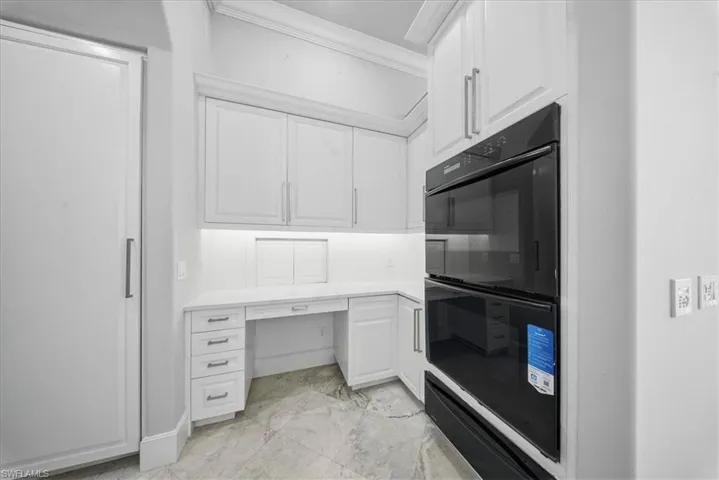 Kitchen featuring white cabinetry, light marble finish floors, ornamental molding, built in desk, and a warming drawer