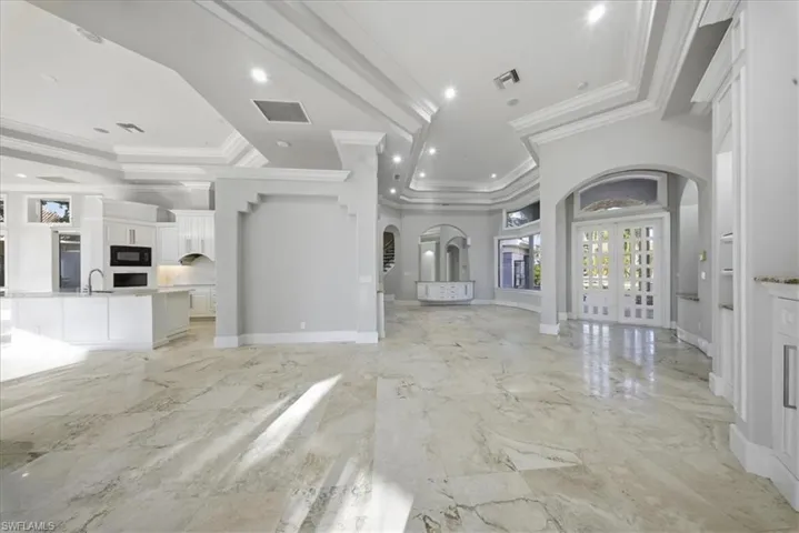 Unfurnished living room featuring arched walkways, french doors, light marble finish floors, crown molding, and recessed lighting