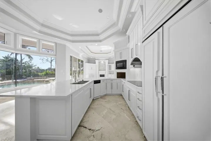 Kitchen featuring ornamental molding, black appliances, white cabinetry, a peninsula, and a raised ceiling
