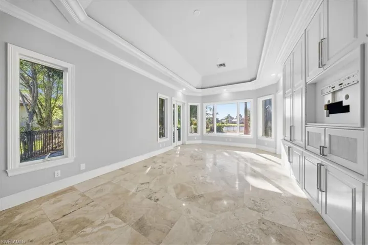 Empty room with ornamental molding, a raised ceiling, light marble finish flooring, and recessed lighting