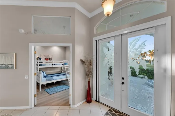 Doorway with crown molding, french doors, and light tile patterned floors