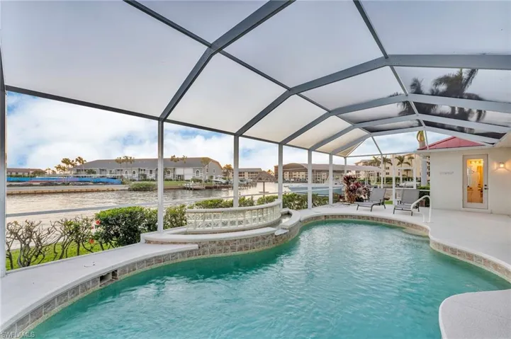 View of swimming pool featuring glass enclosure, a patio area, and a water view