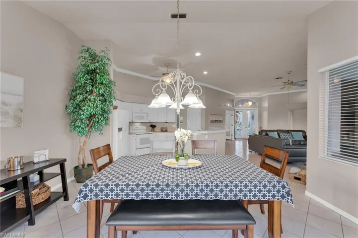 Tiled dining area featuring ceiling fan with notable chandelier and ornamental molding