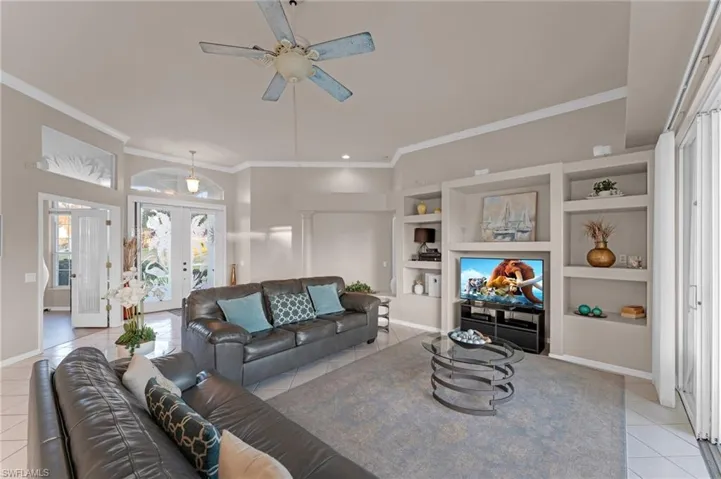 Tiled living room featuring built in shelves, ceiling fan, ornamental molding, and french doors