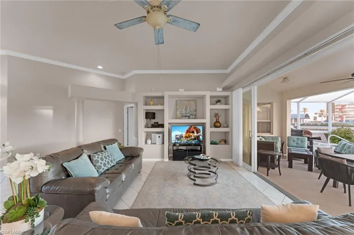 Living room with ceiling fan, light tile patterned floors, and crown molding