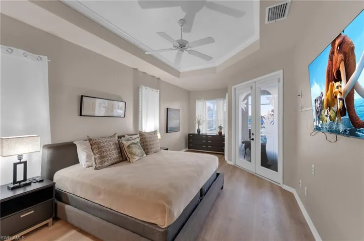 Bedroom with french doors, ceiling fan, access to exterior, light wood-type flooring, and a tray ceiling