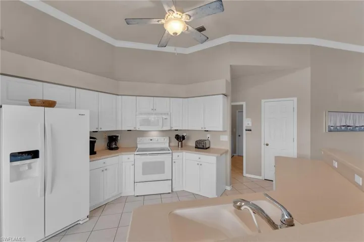 Kitchen with white appliances, white cabinets, sink, ceiling fan, and light tile patterned floors