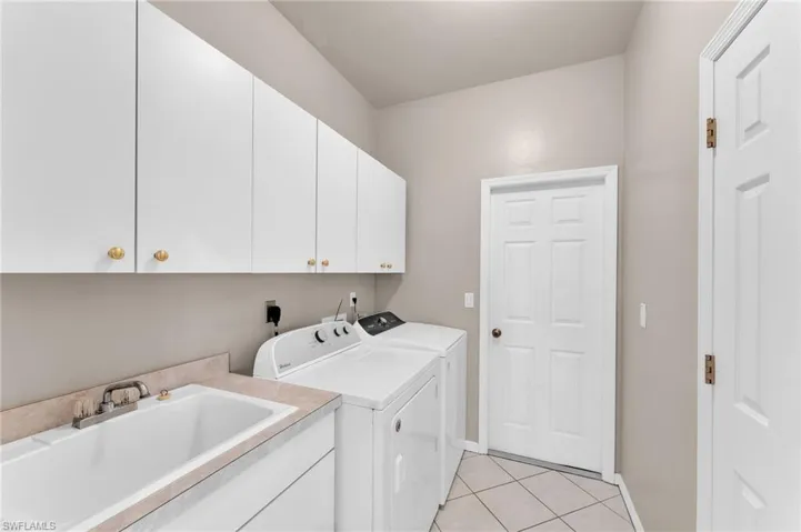 Laundry room with cabinets, independent washer and dryer, light tile patterned floors, and sink