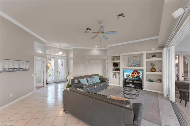 Living room featuring french doors, light tile patterned floors, ceiling fan, and ornamental molding