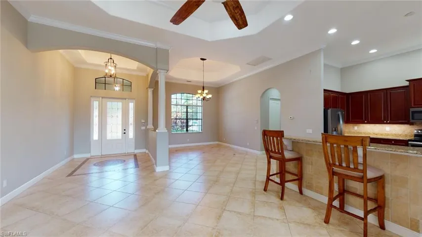 Kitchen with ceiling fan with notable chandelier, appliances with stainless steel finishes, light stone countertops, decorative columns, and a breakfast bar area