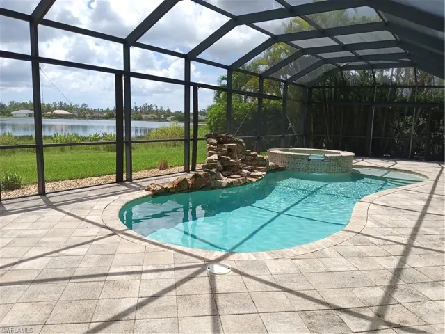 View of pool featuring glass enclosure, a water view, a patio, and an in ground hot tub