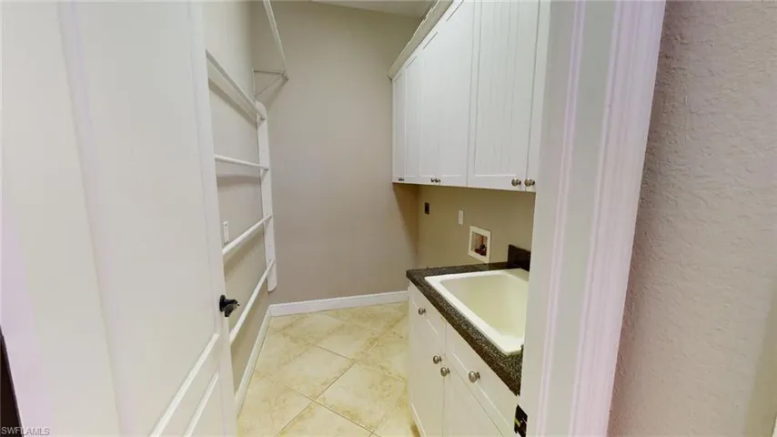 Washroom with hookup for a washing machine, light tile patterned flooring, cabinets, and sink