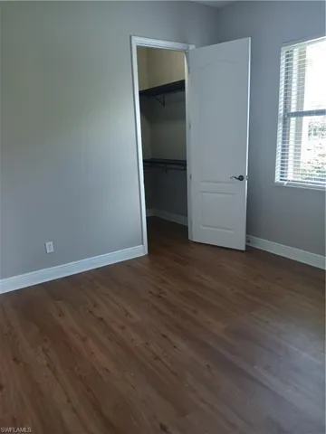 Unfurnished bedroom with a walk in closet, a closet, and dark hardwood / wood-style flooring